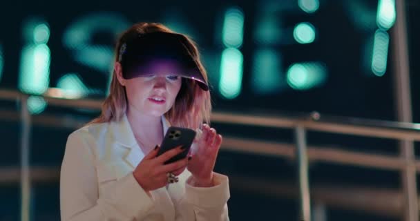 Atrakcyjna kobieta korzystająca z telefonu komórkowego podczas spaceru ulicami nocnego miasteczka 4K - Materiał filmowy, wideo