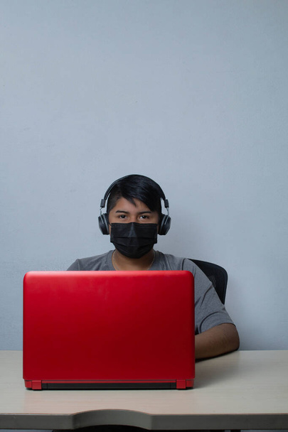 Latino student nosit obličejovou masku, zatímco se on-line třídy videokonference na notebooku pro domácí výuku. mexický muž - Fotografie, Obrázek