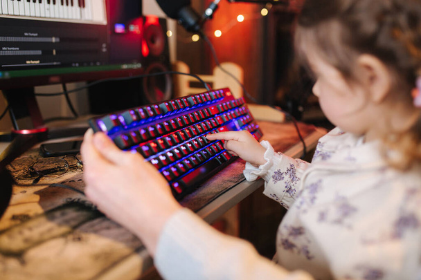 Kardeşine yardım eden kız kardeşi yakın plan ve klavyedeki neon ışıklı düğmeye basıyor. Bilgisayarda çalışan küçük kız. - Fotoğraf, Görsel