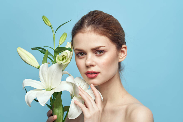 urocza kobieta z białymi kwiatami na niebieskim tle portret przycięty widok - Zdjęcie, obraz