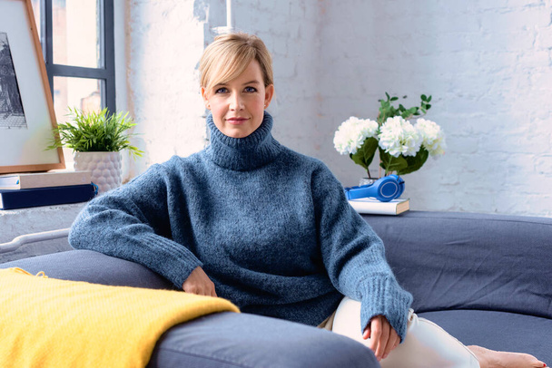 Portrait shot of beautiful blond haired woman wearing turtleneck sweater while relaxing at the couch at home. - Fotoğraf, Görsel