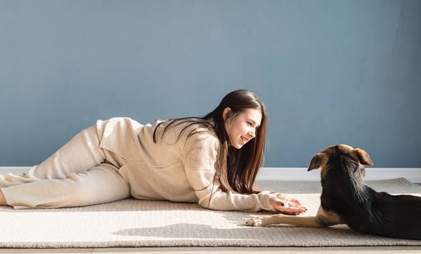 Брюнетка с игривой собакой смешанной породы, веселится и развлекается дома - Фото, изображение