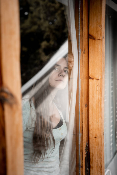 Jovem menina preocupada esperando por alguém olhando pela janela - Foto, Imagem