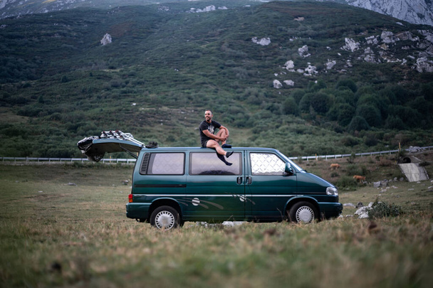 Mladý muž sedí na střeše svého zeleného karavanu uprostřed přírody - Fotografie, Obrázek