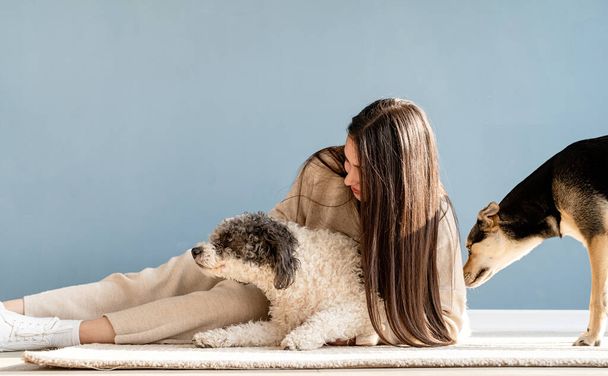 Mooie brunette vrouw met speelse gemengde ras hond, omarmen en plezier hebben thuis - Foto, afbeelding