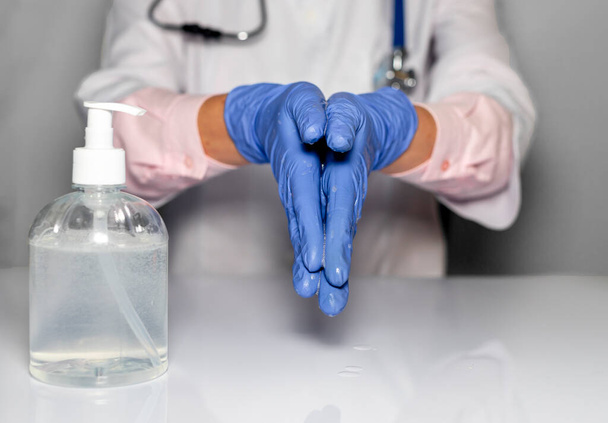 Doctor hands in blue gloves cleaning and washing hands with sanitizer in bottle, close up. - Foto, afbeelding