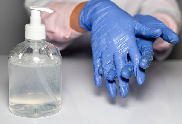 Doctor hands in blue gloves cleaning and washing hands with sanitizer in bottle, close up. - Valokuva, kuva