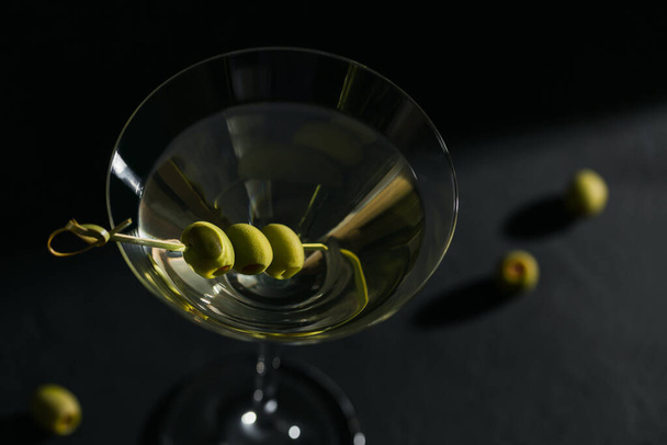 Glass of classic dry martini cocktail with olives on dark stone table against black background. With free space for your text - Foto, Imagen