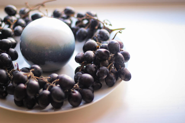 Biała i niebieska kula stoi na środku talerza, a wokół niej są grona winogron. - Zdjęcie, obraz