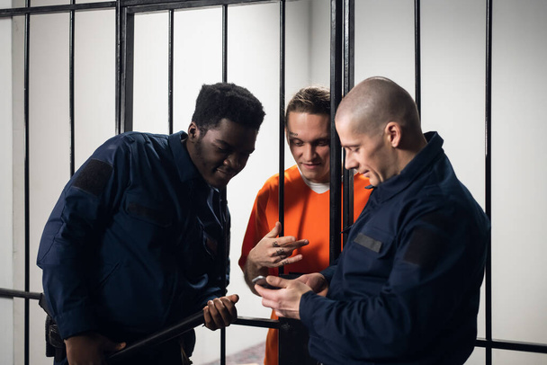 Guardas de prisão e um criminoso perigoso navegam na Internet juntos em um smartphone. - Foto, Imagem