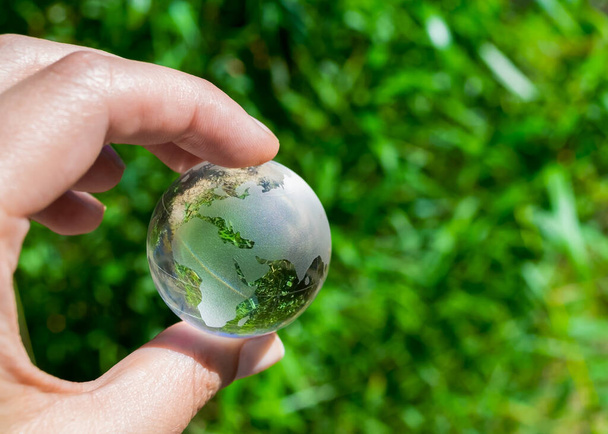 Globo di cristallo nella mano di un uomo su uno sfondo di fogliame verde. Concetto di protezione della Terra. Giornata della Terra - Foto, immagini