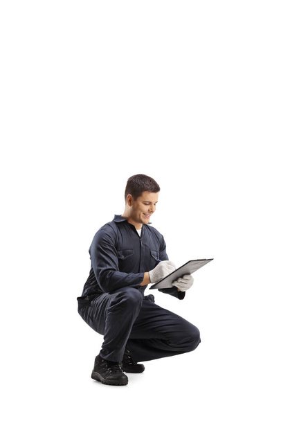 Technician in a uniform kneeling and writing a on a clipboard isolated on white background - Foto, immagini