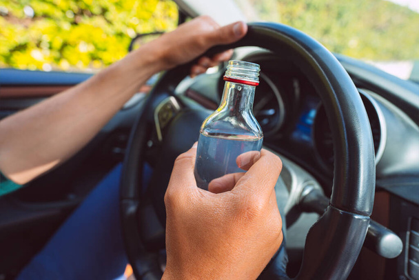 Primer plano del hombre borracho manos en el volante con una botella de vodka. Conducción bajo influencia del alcohol - Foto, Imagen
