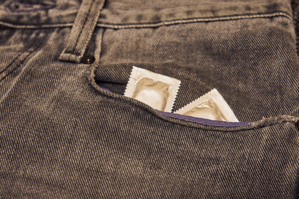 Τα προφυλακτικά είναι στην τσέπη ενός σκισμένου μαύρου τζιν.. - Φωτογραφία, εικόνα