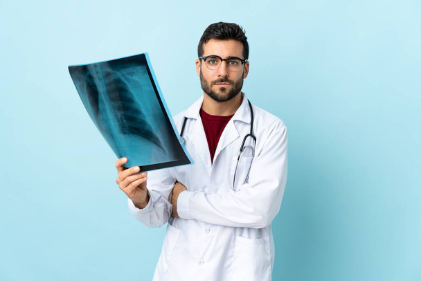Professional traumatologist holding radiography isolated on blue background keeping arms crossed - Foto, Imagem