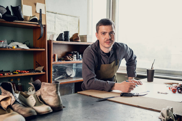 En una zapatería familiar un joven aprendiz trabaja con papel para crear un patrón para zapatos - Foto, Imagen