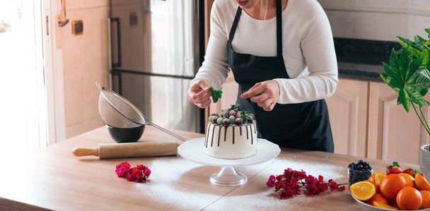 Genç pasta şefi lezzetli ev yapımı beyaz çikolatalı kek pişiriyor ve mutfakta meyveler var. - Fotoğraf, Görsel