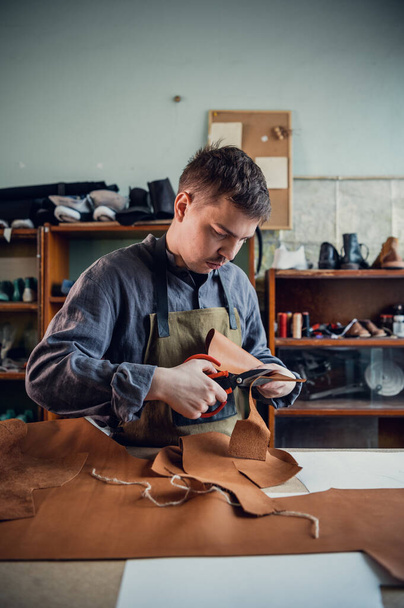 A cipőgyártás mesterkurzusán egy tapasztalt cipész ollóval vágja ki a bőrt. - Fotó, kép