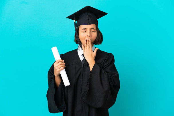 Νεαρή απόφοιτος πανεπιστημίου κορίτσι πάνω από απομονωμένο μπλε φόντο χασμουρητό και καλύπτει ευρύ ανοιχτό στόμα με το χέρι - Φωτογραφία, εικόνα