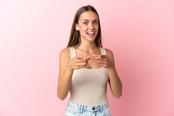 Jonge vrouw over geïsoleerde roze achtergrond verrast en wijzen naar voren - Foto, afbeelding