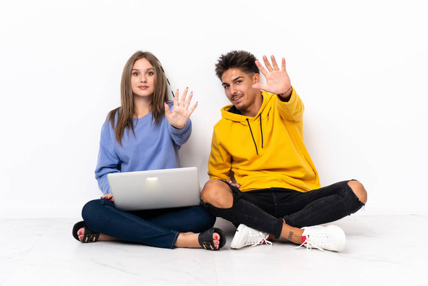 Молодая пара с ноутбуком на полу изолированы на белом фоне, считая пять с пальцами - Фото, изображение