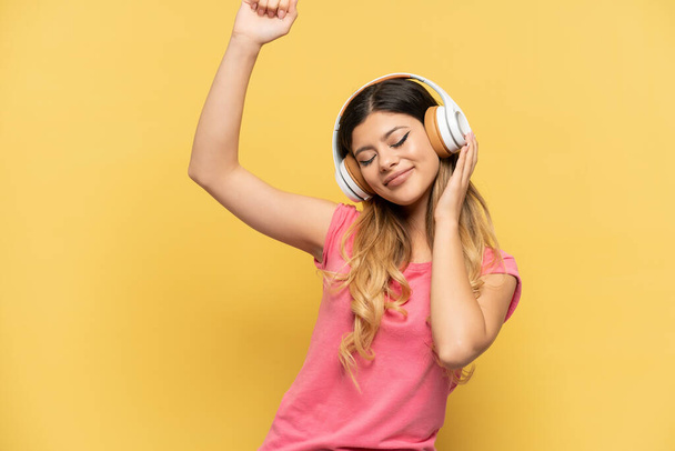 Молода російська дівчина ізольована на жовтому фоні, слухаючи музику і танцюючи - Фото, зображення