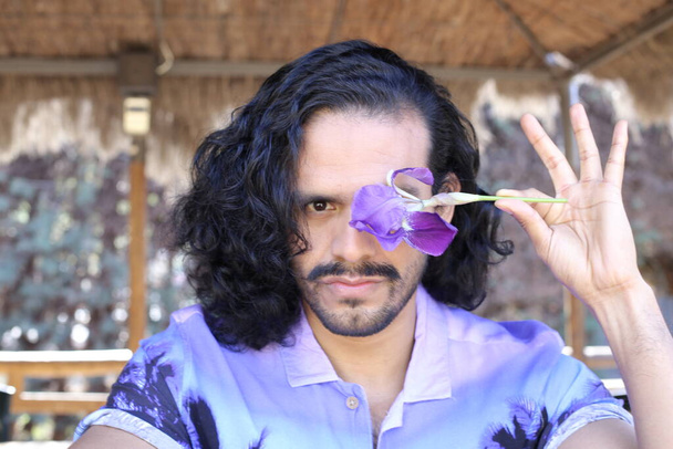 portret van knappe jongeman in stijlvol paars shirt met orchidee bloem buiten - Foto, afbeelding
