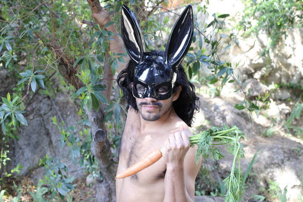 muotokuva komea nuori paidaton mies musta pupu naamio tilalla porkkana metsässä - Valokuva, kuva