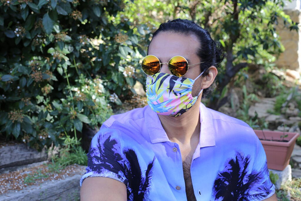 portrait of handsome young man in stylish purple shirt, breath mask and sunglasses outdoors - Photo, Image