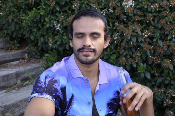 retrato de joven guapo en camisa púrpura con estilo con botella de cerveza al aire libre - Foto, Imagen