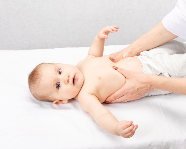 Ένα κοριτσάκι έξι μηνών που κάνει μασάζ στην παιδιατρική κλινική. Χειρωνακτικός θεραπευτής χειρίζεται την κοιλιά και το στήθος του παιδιού - Φωτογραφία, εικόνα
