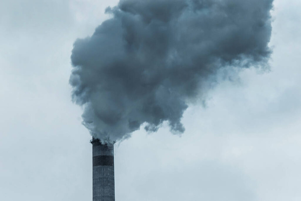Milieuverontreiniging en ecologie. Donkergrijze zure rook komt uit een schoorsteen van een industriële installatie of thermische centrale tegen de achtergrond van de lucht. - Foto, afbeelding