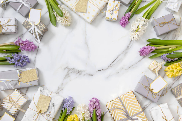 Top view trendy composition with festive wrapped gift boxes ribbon bow decorated by bloom flowers. Stylish packing presents with natural blossom on white marble. Beautiful holiday celebrating - Foto, afbeelding
