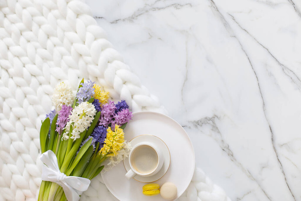 Top view composition with cup of coffee and spring multicolored hyacinth on white fluffy knitted plaid. Beautiful accessories relaxing time for yourself with blossom flowers and hot drink beverage - Foto, afbeelding