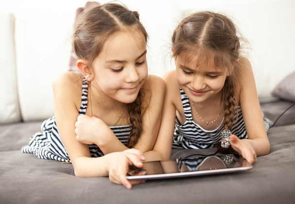lachende schoolmeisjes liggend op de Bank en spelen op Tablet PC - Foto, afbeelding