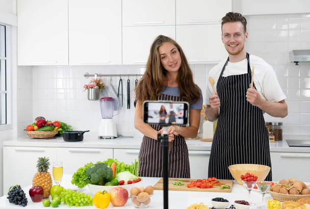 young caucasian couple who are blogger teaching people to cook healthy food via smartphone camera. family together concept - Photo, Image