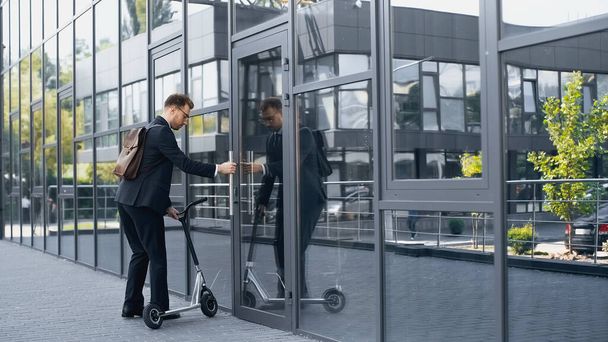 бізнесмен в костюмі і рюкзаку ходить в будівлі з електричним скутером
  - Фото, зображення