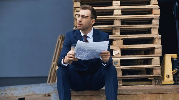 businessman sitting while holding coffee to go and newspaper outside  - Photo, image