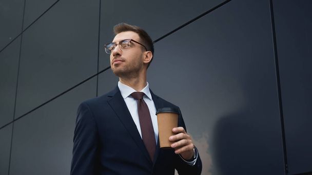 businessman in formal wear holding coffee to go and looking away outside  - Foto, imagen