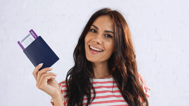 positive woman holding passport with air ticket while looking at camera - Foto, afbeelding