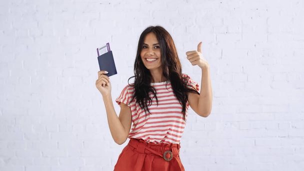 fröhliche Frau hält Pass mit Flugticket und zeigt Daumen hoch - Foto, Bild