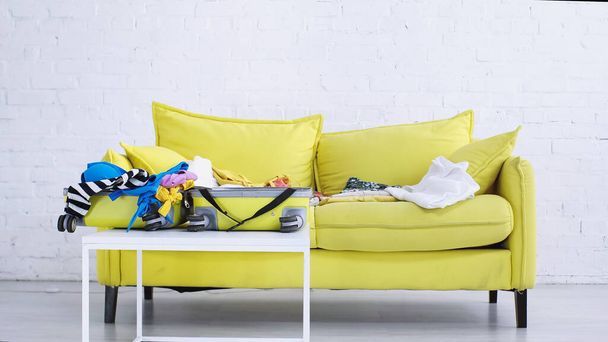 сумка с повседневной одеждой на кофейном столике рядом с желтым диваном  - Фото, изображение