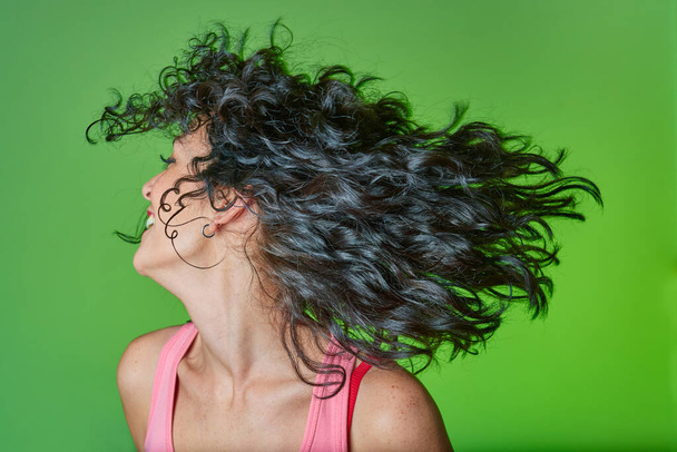 smiling young woman with curly black hair following curly girl method for caring for her curls and hair. hair care concept. green background. - Photo, image