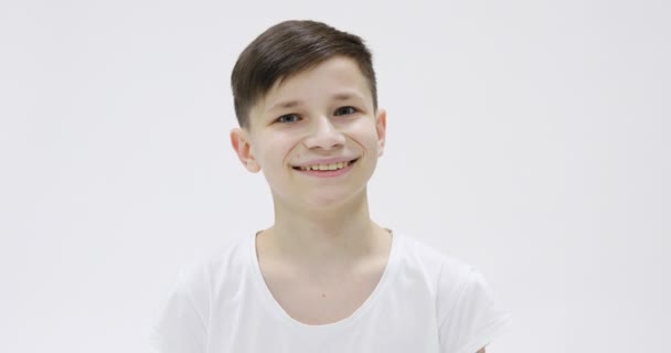Όμορφος έφηβος 14s σε λευκό t-shirt ευτυχώς χαμογελαστός απομονωμένος πάνω από λευκό φόντο στο στούντιο. Άνθρωποι ειλικρινή συναισθήματα, έννοια του τρόπου ζωής. Κοιτάζοντας την κάμερα με γοητευτικό χαμόγελο, έκπληξη - Πλάνα, βίντεο
