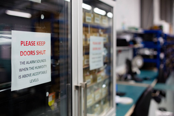 Großaufnahme eines Schildes an einem feuchtigkeitsempfindlichen Schrank eines Elektronikherstellers, das die Menschen warnt, Türen geschlossen zu halten, um die Rohkomponenten im Inneren zu schützen - Foto, Bild