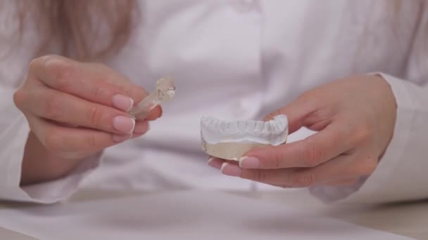 Una mujer ortodoncista sostiene en su mano un plato para corregir los dientes y la oclusión. Poner la plancha sobre los dientes blancos de yeso. Tratamiento de la mandíbula en un consultorio médico especializado. Un saludable y hermoso - Metraje, vídeo