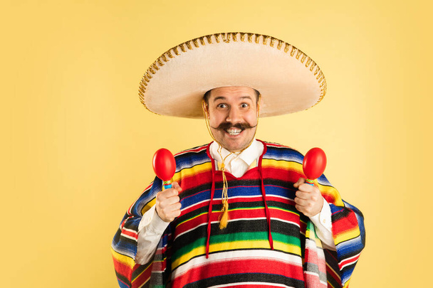 Happy man in sombrero and bright poncho isolated over yellow background - Photo, Image