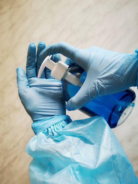 Um par de mãos em luvas de borracha azul pulveriza as mãos com um spray higiênico. Isolado em branco com caminho de recorte, copie espaço para o seu texto. Limpeza geral em uma empresa de limpeza comercial - Foto, Imagem