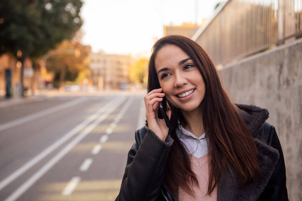 portrait of a young smiling woman making a phone call while walking down the street, concept of technology and urban lifestyle, copyspace for text - Foto, imagen