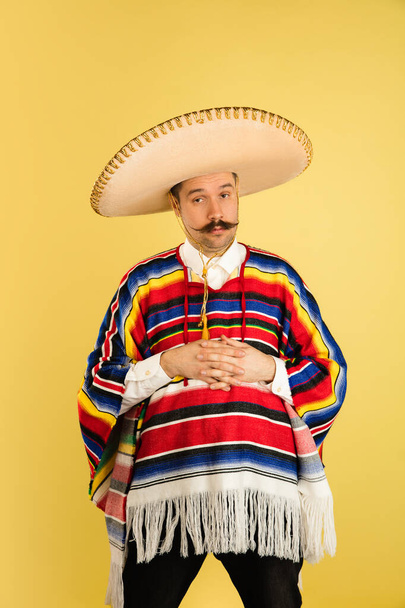 Portrait of sad man in bright garment and sombrero isolated on yellow background - Photo, Image